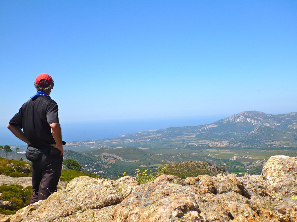 A hiker at a sunny, exposed viewpoint above the Corsican coast on the GR20